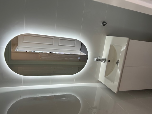 renovated bathroom with an oval mirror, glossy floor, and white vanity unit.